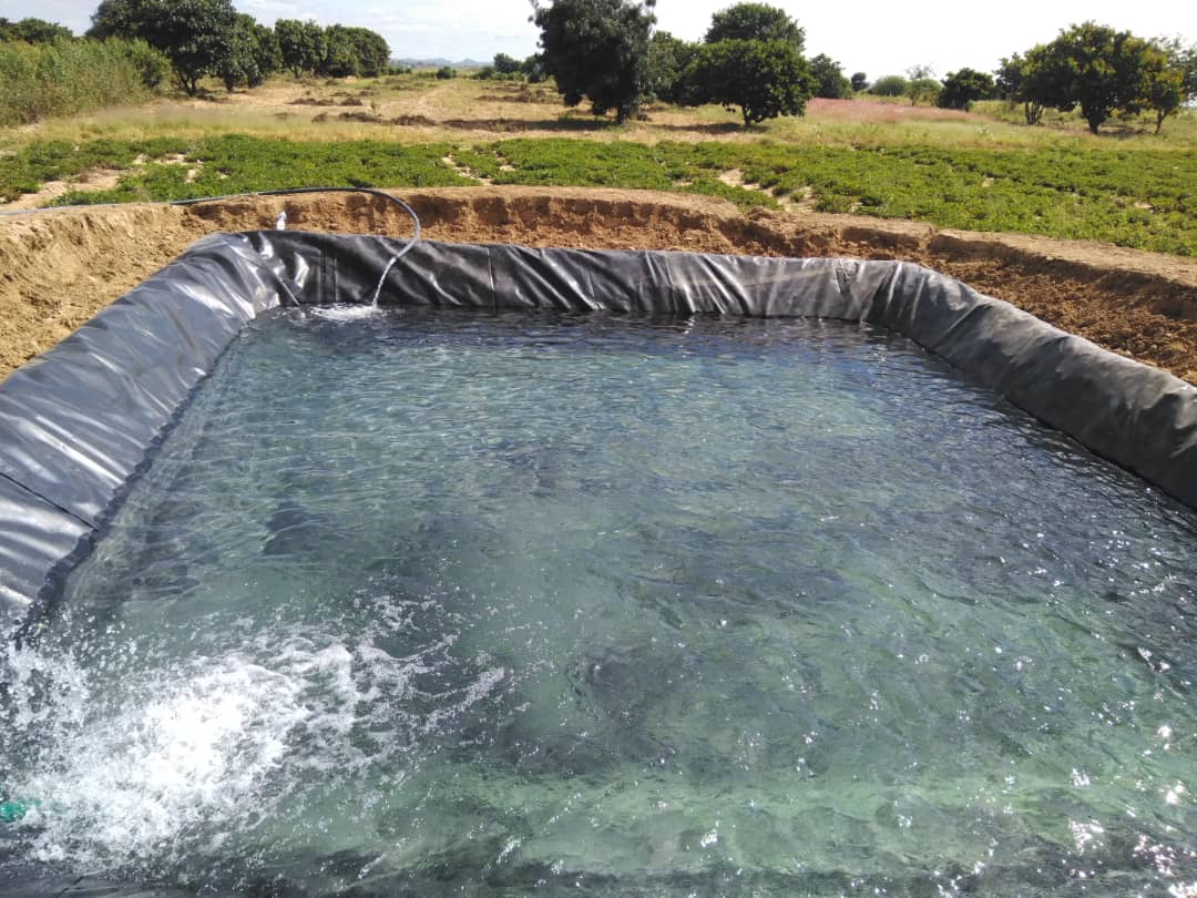 Completed irrigation reservoir with water flowing in farm landscape